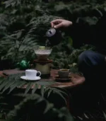 A wide shot of someone drinking coffee from a teacup and saucer outdoors